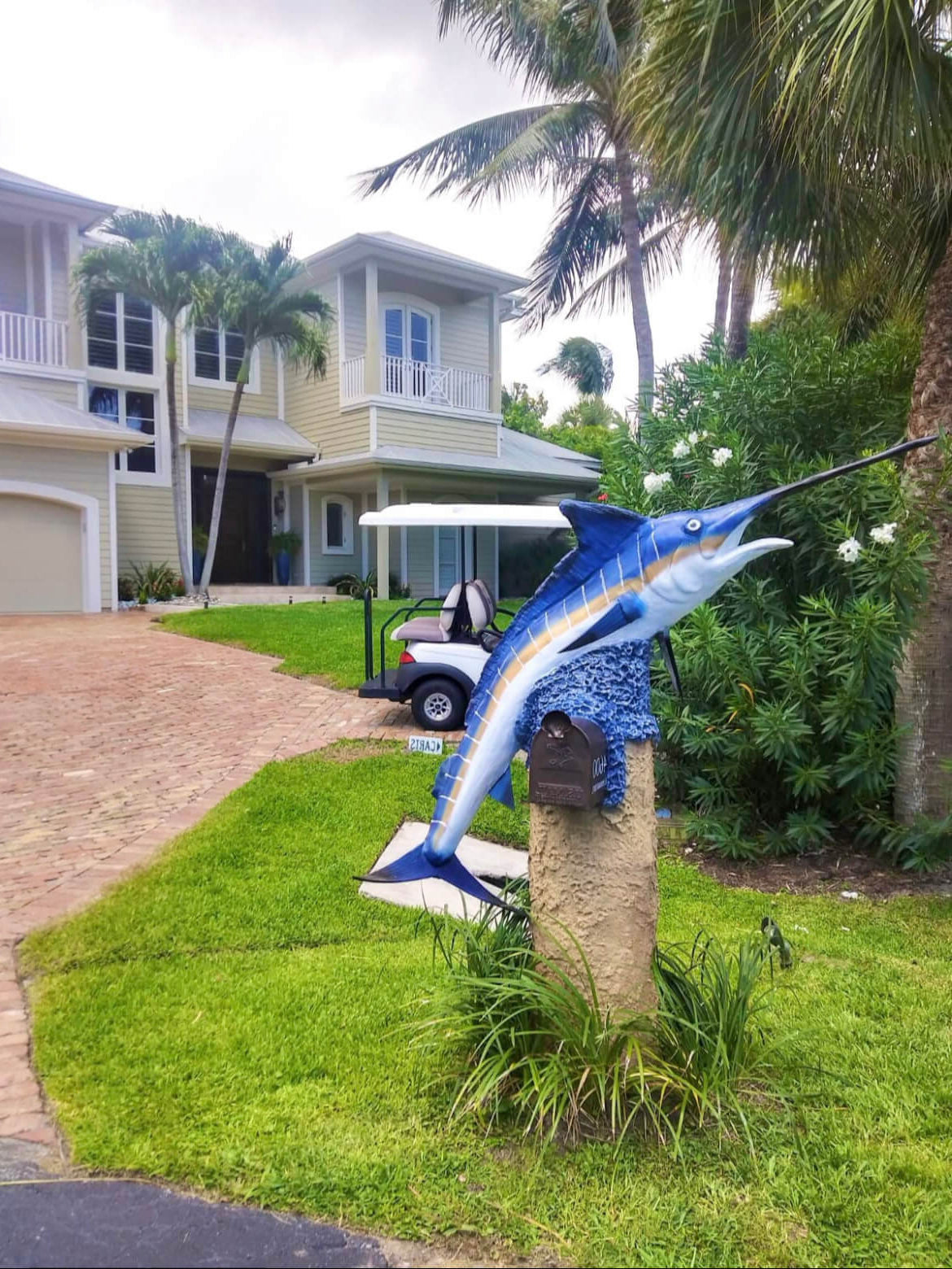 Blue marlin sculpture on a grassy lawn with a house in the background