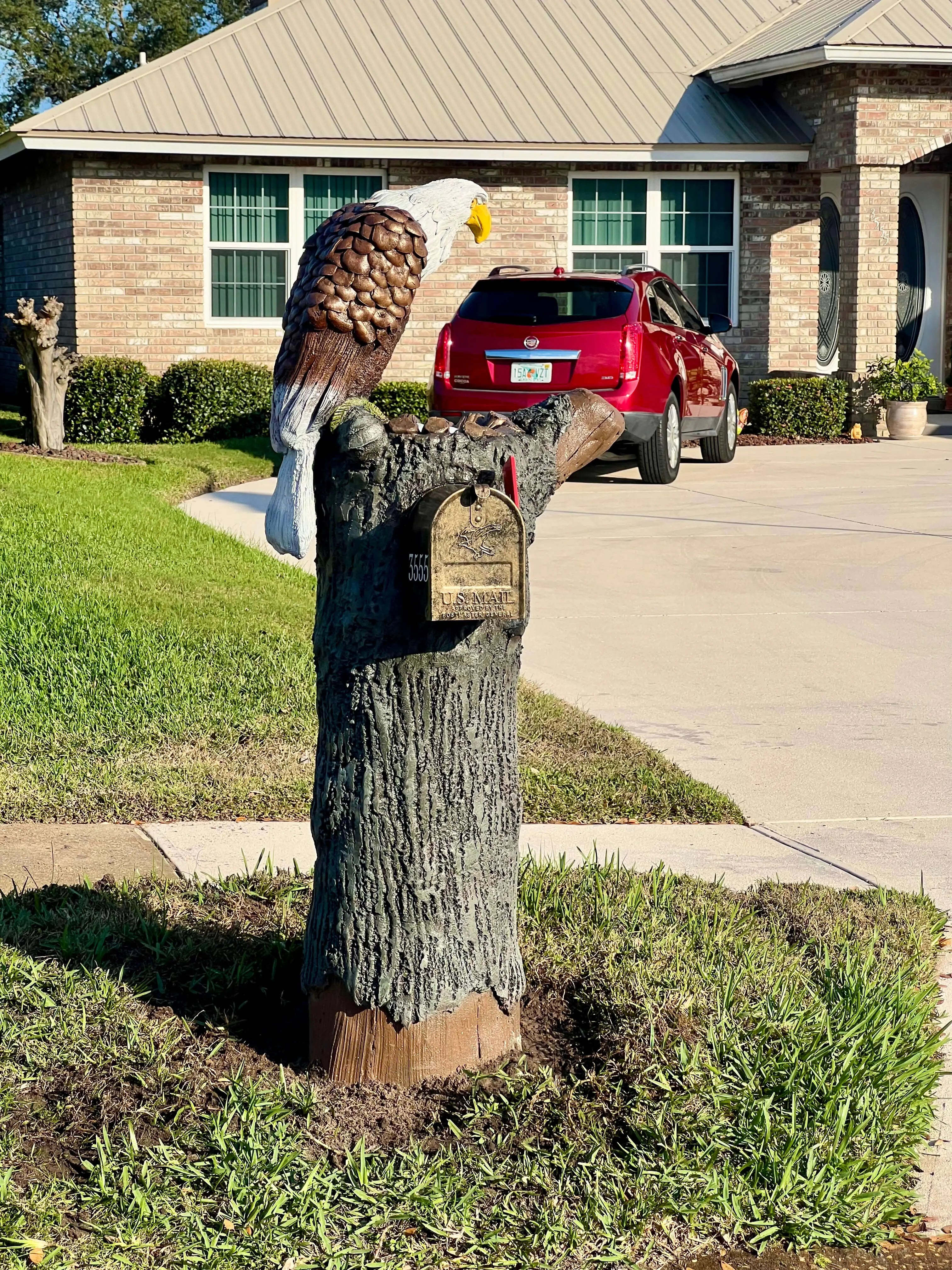 Decorative mailbox shaped like a tree stump with an eagle on top, in front of a house.
