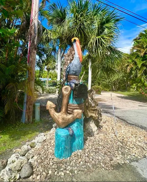 Decorative sculpture of a pelican and anchor in a tropical setting with palm trees and clear blue sky.