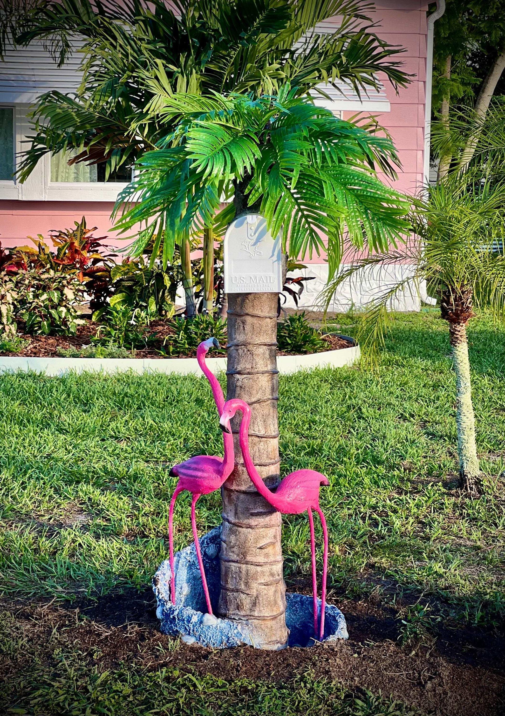 Decorative flamingo mailbox statues on a palm tree trunk with a pink house in the background in Florida