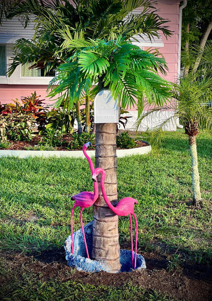 Decorative flamingo mailbox statues on a palm tree trunk with a pink house in the background in Florida