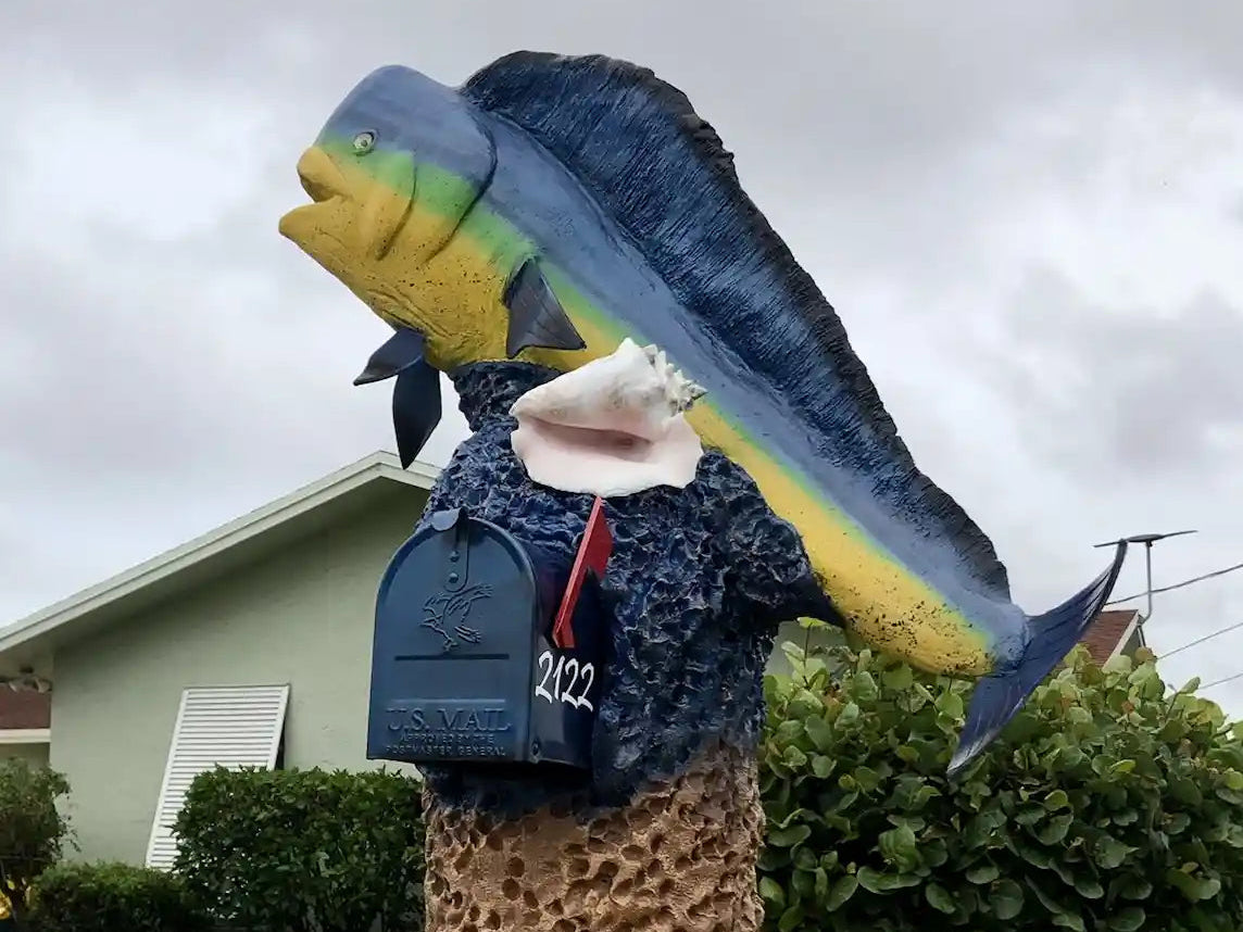 Decorative mailbox shaped like a fish with a house in the background