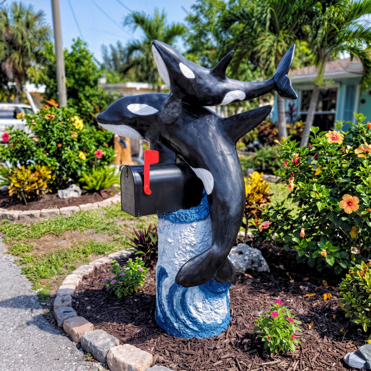 Orca mailbox sculpture with baby orca and black mailbox in a tropical garden